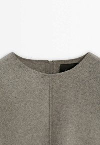 Gros plan sur l'encolure d'une robe en laine grise avec une fermeture éclair invisible dans le dos et un détail de couture centrale.