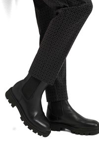 Zwarte leren Chelsea-laarzen met elastische zijpanelen, robuuste rubberen zool en contrasterende zwart-gepatenteerde broeken met textuur.