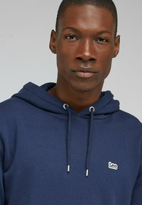 Granatowy kaptur z bawełnianej mieszanki, z małym białym logo "Lee" na lewej piersi i regulowanym sznurkiem w kapturze.