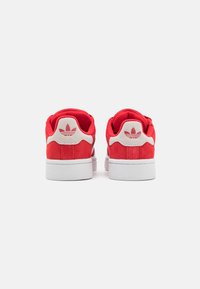 Zapatillas de ante rojas con suelas de goma blanca, con una textura suave, forma redondeada y un sutil logo en relieve en el talón.