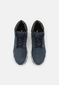 Granatowe zamszowe sneakersy z czarnymi skórzanymi akcentami, okrągłym noskiem i płaskimi sznurowadłami. Biała gumowa podeszwa z minimalnym wzorem bieżnika.