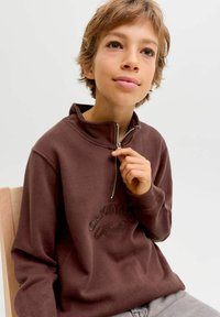 Sweat à zip marron avec un col haut et un texte brodé "Originals" sur la poitrine, en matériau doux, associé à un pantalon gris.