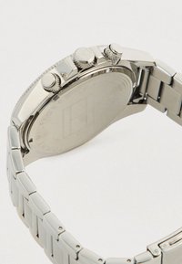 Rustfrit stål armbåndsur med metal link bånd, der har tre strukturerede justeringskrone og graveret bagside.