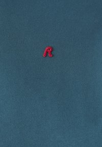 Turkis bomull t-skjorte med ribbet tekstur; har et rødt broderi "R"-logo på venstre brystområde.