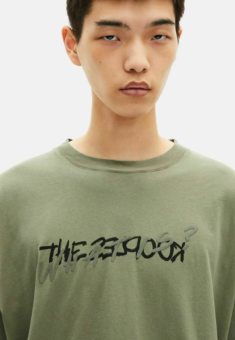 Sudadera de algodón color verde oliva con un corte relajado, que presenta un gráfico de texto abstracto en negro y gris en el frente. Cuello redondo y tejido texturizado.