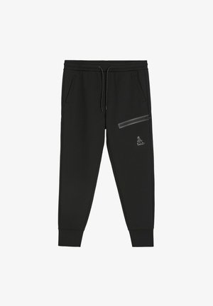 Czarne dresy wykonane z miękkiego materiału, z regulowanym paskiem w talii, bocznymi kieszeniami oraz kieszenią na zamek błyskawiczny z odblaskowym detalem.