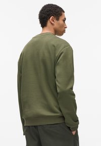 Sudadera verde oliva con un corte relajado, cuello redondo y puños de canalé. Tela suave con detalles de costura mínimos.