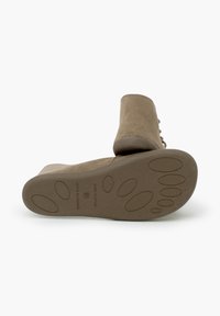 Beige suède enkellaarsje met een ronde neus, gladde textuur en een rubberen zool met cirkelvormige grippatronen. "Made in Spain" label op de zool.