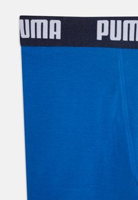 Modre bokserice z črnim elastičnim pasom, na katerem je v beli barvi napis "PUMA". Gladka tekstura, prilegajoča zasnova in okrepljeni šivi.