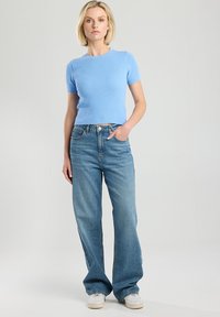 Light blue ribbed short-sleeve sweater paired with high-waisted light blue straight-leg jeans, worn with cream footwear. Simple design.
