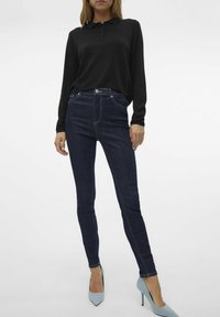 Crna majica s dugim rukavima i tri gumba, uparena s tamnoplavim trapericama. Obuća se sastoji od svijetloplavih šiljastih potpetica. Jednostavan i prilagođen dizajn.