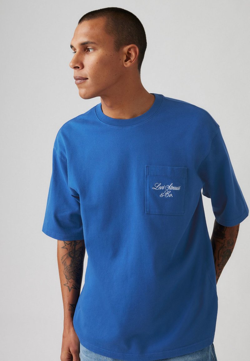 Μπλε βαμβακερή μπλούζα με κοντά μανίκια και τσέπη στο στήθος, διακοσμημένη με κεντημένο λογότύπο "Levi Strauss & Co.". Απαλή υφή, χαλαρή εφαρμογή.