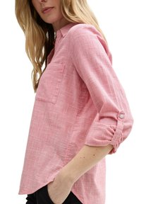 Camicia a righe rossa e bianca con taschino sul petto e maniche arrotolate a 3/4, realizzata in tessuto leggero. Texture morbida e vestibilità comoda.