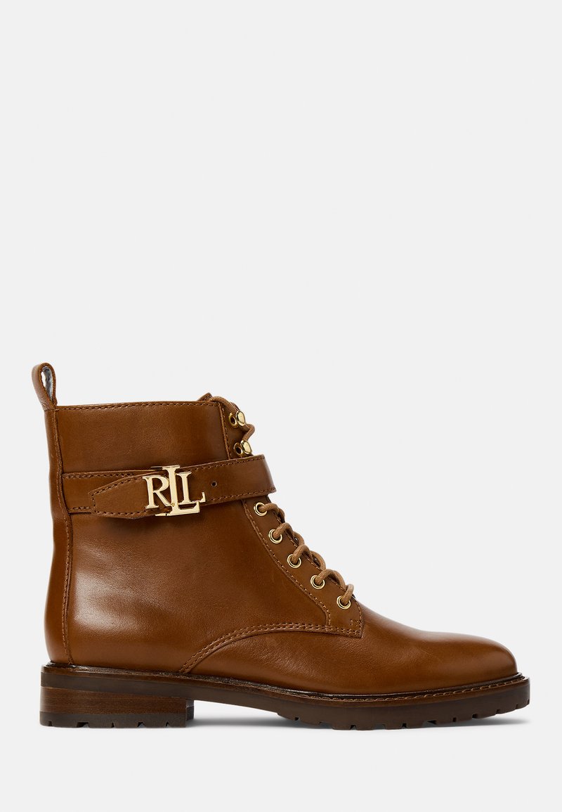 Bota ankle em couro castanho com atilhos na parte da frente, ferragens douradas, tira lateral com detalhe do logótipo e um salto plano. Textura suave e design resistente.