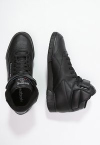 Baskets montantes noires avec tige en cuir, col rembourré, lacets plats et semelle en caoutchouc. Présente l'emblème Reebok et une sangle ajustable.