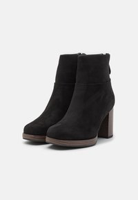 Black suede ankle boots featuring a rounded toe, a wide block heel, and a subtle zipper detail at the back. Textured wooden heel.