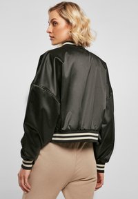 Veste bomber en satin noir avec des manches bouffantes, des bords-côtes rayés aux poignets et à la taille. Texture lisse avec une coupe cropped et décontractée.