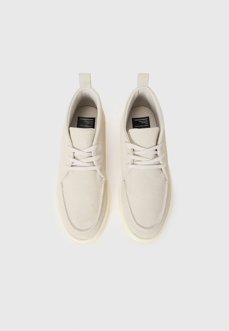 Baskets en suede beige clair avec un bout arrondi, des lacets blancs et une languette au talon. Texture douce et semelle en caoutchouc crème.