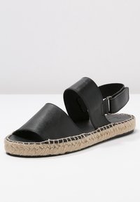 Černá kožená espadrilová sandál se otevřenou špičkou, širokými pásky na svršku, nastavitelným nártem a juty omotanou podrážkou.