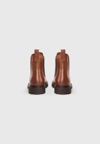 Brown leather ankle boots with elastic side panels, pull tabs, and black rubber soles, showing a smooth texture and rounded shape.