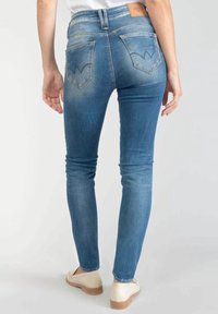 Jeans skinny blu in denim, con vita alta, aree scolorite e un design unico delle tasche posteriori con un motivo distintivo.