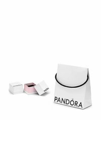 Kleine weiße Pandora-Schmuckkästchen, wobei eines geöffnet ist und ein pinkfarbenes Innere zeigt, neben einer weißen Pandora-Einkauftasche mit schwarzen Griffen.