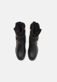 Bottines en cuir noir avec une doublure en fourrure noire duveteuse en haut. Sangle ajustable avec un accent doré. Texture lisse et bout rond.
