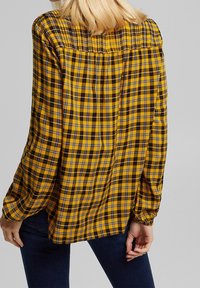 Camicia a quadri gialla con maniche lunghe, caratterizzata da un design con schiena arricciata e dettagli a scacchi bianco e nero, realizzata in tessuto morbido.