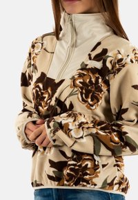 Pullover in pile con motivo floreale in beige, marrone e verde. Caratterizzato da un collo con zip a metà e una texture morbida. Logo Columbia sul petto.