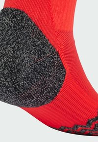 Calcetín rojo con secciones de talón y puntera en negro texturizado. Presenta un borde superior acanalado y un diseño decorativo a lo largo del borde inferior.