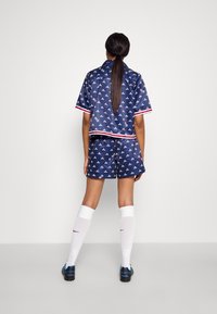 Set sportivo a motivi navy con top a maniche corte e pantaloni corti, con accenti bianchi e rossi. Indossato con calze bianche fino al ginocchio e scarpe nere.