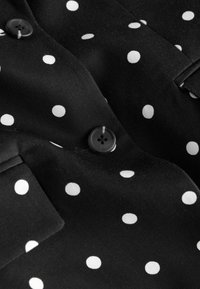 Tissu noir à pois blancs avec deux boutons noirs et un détail de col.