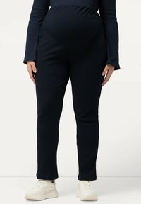 Marina-ribbade gravidbyxor med elastisk midja, slim fit och något utflutande nederkant. Bärs med ljusa sneakers.