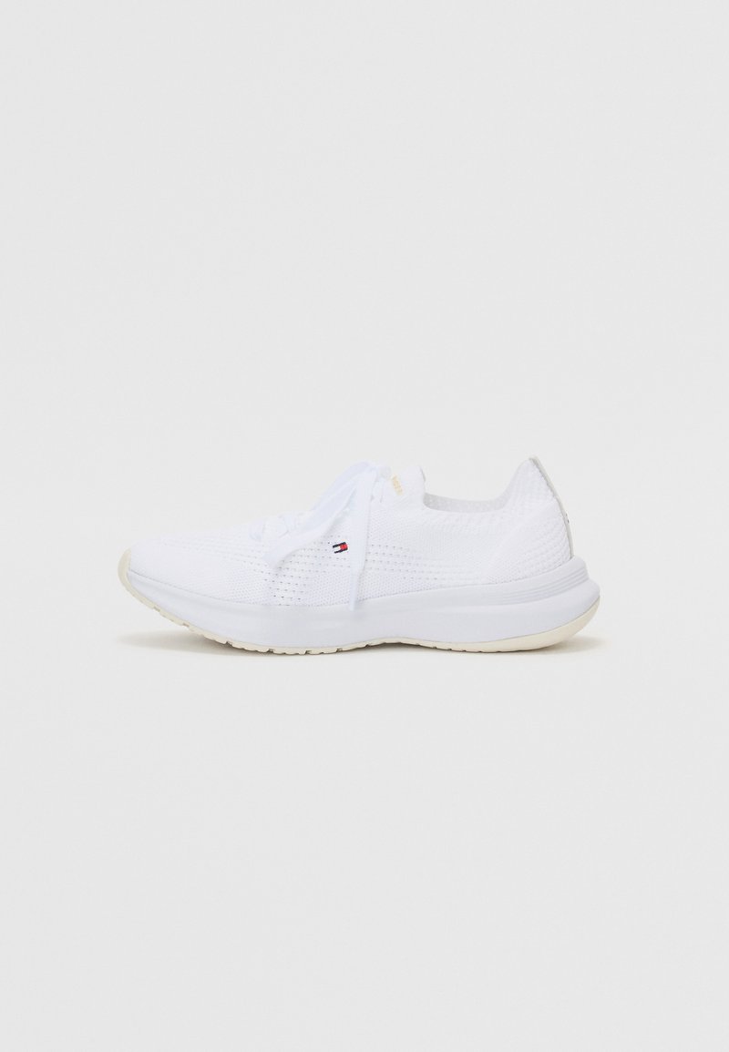 White athletic shoe with a textured upper, round toe, and contrasting sole. Features lace-up closure and subtle branding on the side.
