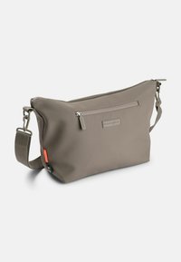 Taupe crossover taske med justerbar rem, frontlomme med lynlås og små brandtags på siden mod en ensfarvet hvid baggrund.