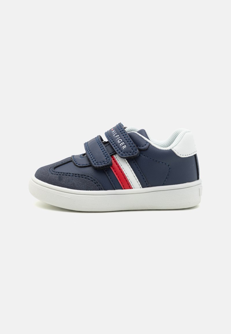 Baskets pour enfants en bleu marine avec deux bandes Velcro réglables, rayures blanches et rouges, col rembourré et semelles en caoutchouc texturé.