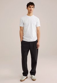 Camisa blanca de manga corta, pantalones oscuros de corte holgado y zapatillas gris con acentos blancos. Diseño simple y casual, textura suave.
