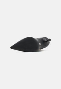 Chaussure noire à bout pointu avec une surface en cuir lisse, une semelle texturée et un accent noir saillant distinctif au talon.