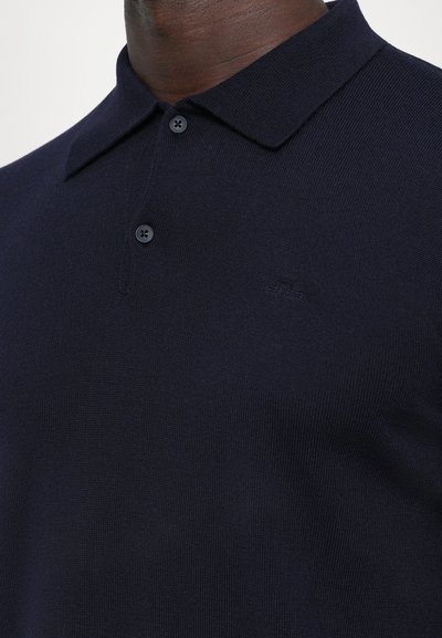Mörkblå polo t-shirt i strukturerad tyg, med klassisk krage, två knappslå och diskret logotypdetalj på bröstet.