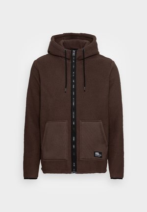 Felpa con zip marrone in pile con coulisse nere, due tasche a toppa anteriori e una piccola etichetta nera "Rebel" sulla tasca inferiore destra.