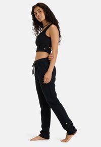 Black fitted crop top with cut-out detail and silver accent, paired with black elastic waist pants featuring adjustable drawstring and side button.