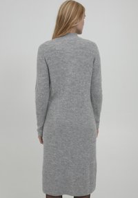 Abito grigio a maglia con texture a costine, maniche lunghe e collo alto. Arriva sotto il ginocchio con spacchi laterali per facilitare i movimenti.