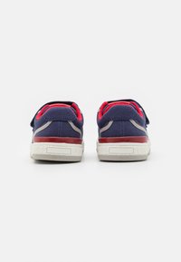Marineblå kanvas sneakers med en rød aksentkant, grå sidestykker og en hvit strukturert gummisåle. Bakfra er det en visning som viser doble reimer.