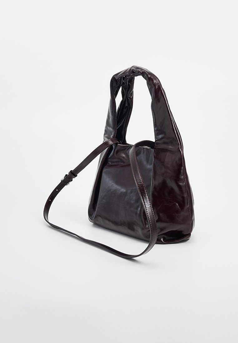 Sac en cuir marron foncé au design décontracté, doté d'une seule sangle ajustable et d'une texture lisse et brillante.