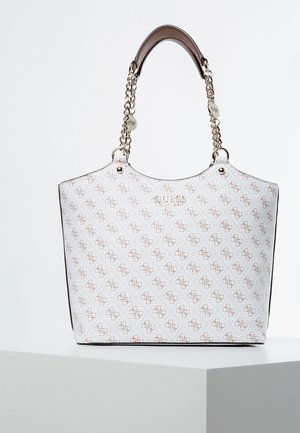 Sac fourre-tout blanc Guess avec motif logo marron, chaîne dorée et poignées en cuir, présenté sur un socle blanc sur un fond uni.