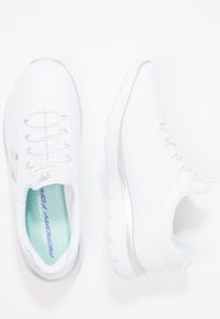 Vita sportskor i vitt med texturerad mesh-övre, silverdetaljer och snörning. Det vadderade inre har en "Skechers Memory Foam"-etikett.