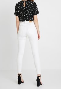 Blusa negra de manga corta con estampado de pájaros blancos, con apertura en la espalda; combinada con jeans skinny blancos y sandalias de tacón negras.