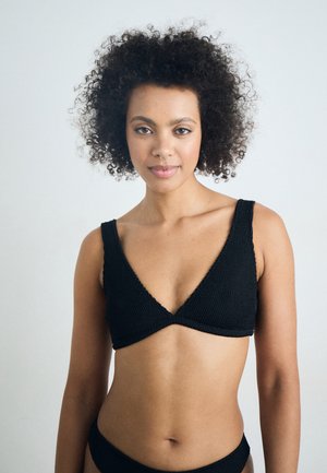 Black knit bralette with wide straps and a deep V-neck. Textured material and seamless design, paired with a matching bottom.