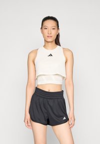 Haut de sport blanc court avec un design texturé et un logo noir, associé à un short noir taille haute avec une taille élastique et un logo.