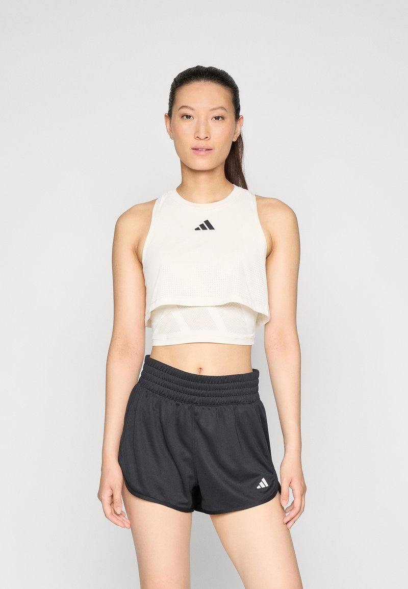 Hvid cropped atletisk top med et struktureret design og sort logo, parret med højtaljede sorte shorts med elastisk talje og logo.